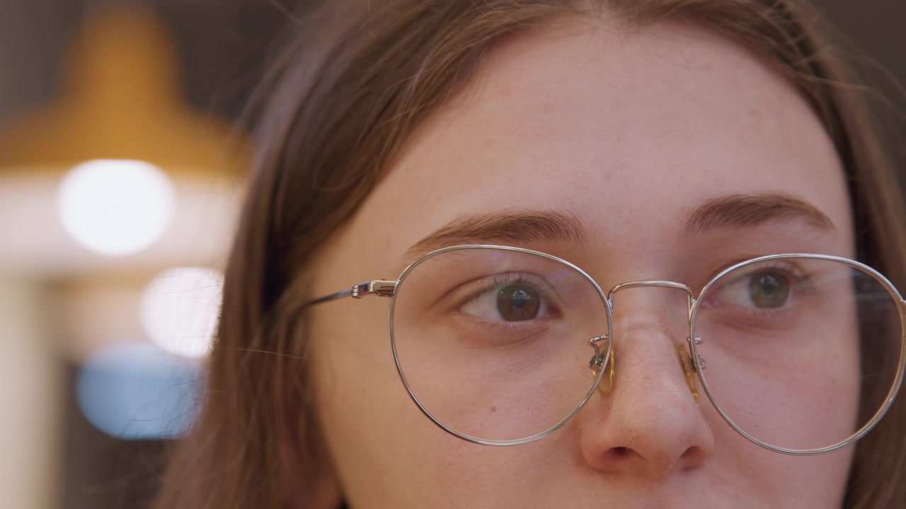 Giovane cliente caucasica che prova montature di occhiali in una boutique, che si guarda allo specchio con uno sguardo contemplativo, luci bokeh soffuse e riflesso sottile, momento di attenta prova prima dell'acquisto.