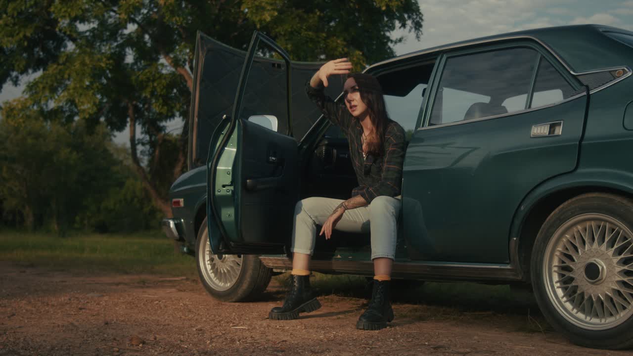 Woman Sitting Beside a Vintage Car in Nature
