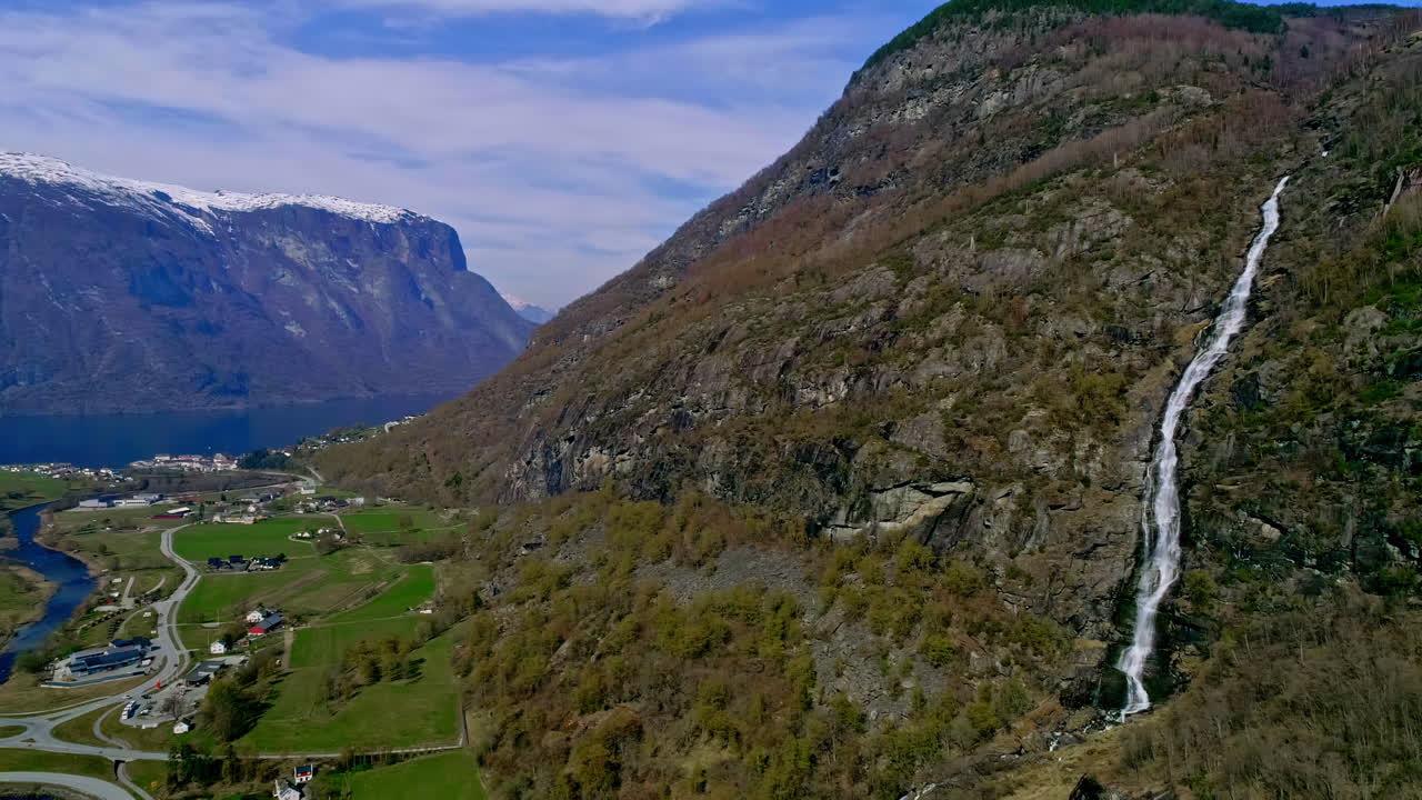 toma en ángulo alto de la hermosa cascada por las montañas rocosas en aurland, noruega con la vista de las casas de la ciudad debajo durante el día