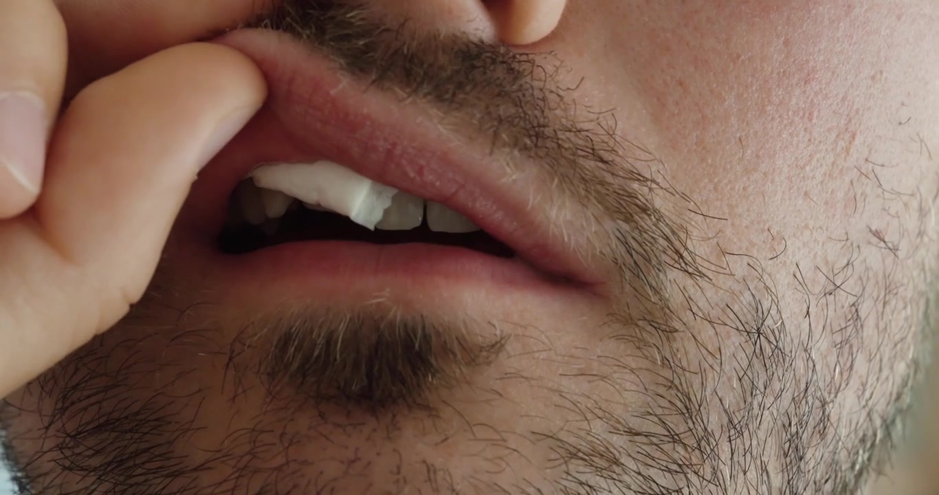 Extreme close up of a man using his fingers to position a small snus pouch beneath his lower lip