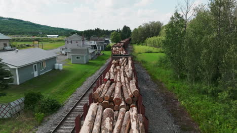low aerial view of stationary freight train loaded with lumber, adjacent to residential homes in rural maine