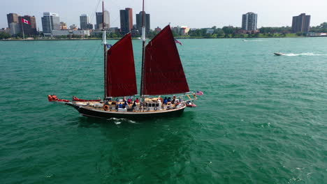 Aerial-tracking-shot-in-front-of-a-tall-ship,-sailing-on-the-Detroit-river-with-Windsor-background