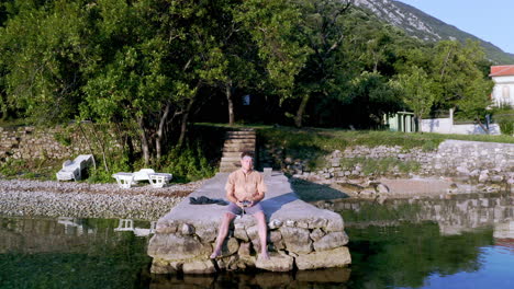 Zoom-out-shot-of-a-young-man-lying-on-a-stone-pier-in-the-Kotor-bay-in-Montenegro