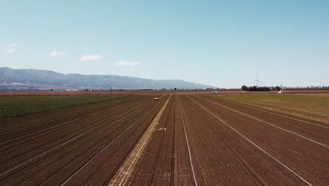 Slow-Motion-wide-drone-HIGH-ANGLE-of-artichoke-farm-field-and-weeding-machine-moving-forwards-towards-road