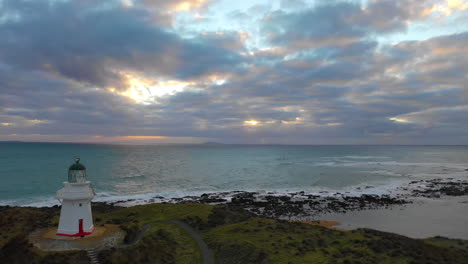 vista aérea del faro de waipapa mientras el sol se pone detrás de las nubes a lo largo de la pintoresca costa de nueva zelanda