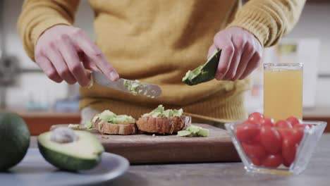 sección media de un hombre caucásico preparando tostadas de aguacate en la cocina, cámara lenta