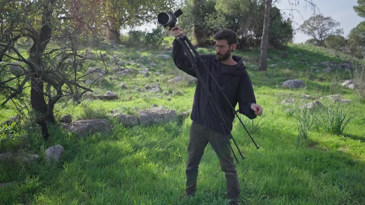 Videografo che apre le gambe del treppiede e lo posiziona sull'erba in una radura nella foresta.