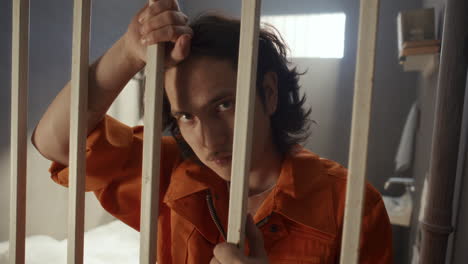 Portrait of Young Male Inmate Leaning on Bars in Jail Cell
