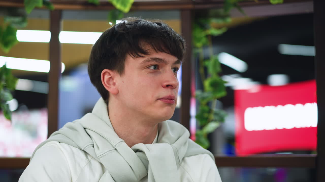 white student engaged in conversation with colleague near red beam background, casual indoor setting, expressive face and hand gesture, youthful peer interaction captured from medium close angle