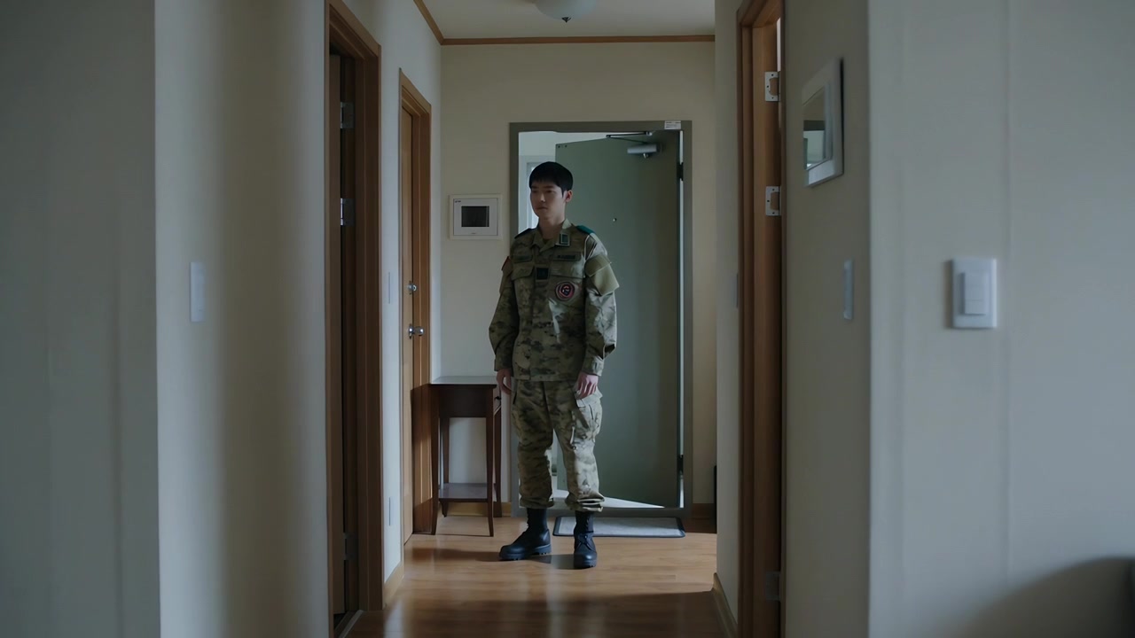 Soldato in piedi in mimetica militare scruta un corridoio residenziale stretto, sorvegliando la porta d'ingresso.