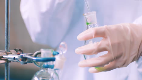 medical staff use suction pipette dispensing green liquid to a tissue culture flask with suction pipette for cell culture assay in biological cabinet on in cleanroom environmental facility laboratory.