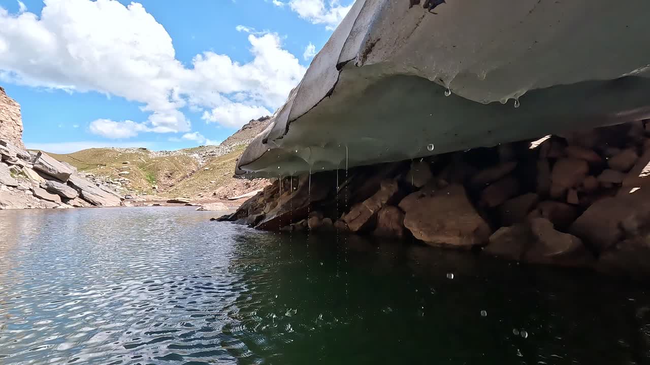 Snowbank melting into a crystal-clear alpine pool surrounded by rocks in Alpe Veglia Natural Park, Piedmont, Italy