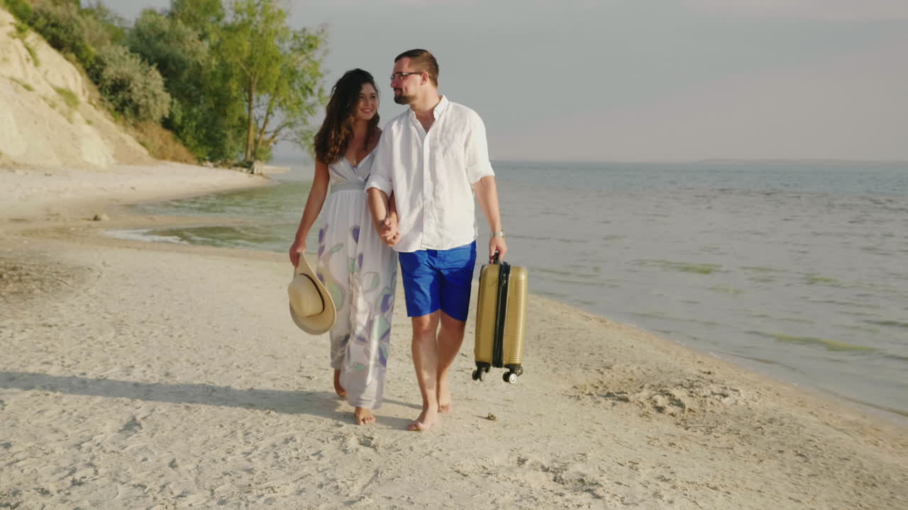 una pareja amorosa camina por una playa tropical y lleva una bolsa de viaje con una toma de steadicam