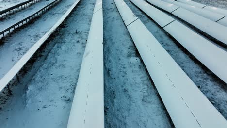 aerial tracking shot low over snow covered solar panels, winter evening