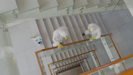 top view of two cleaning men wearing personal protective equipment cleaning stair railings inside an office building