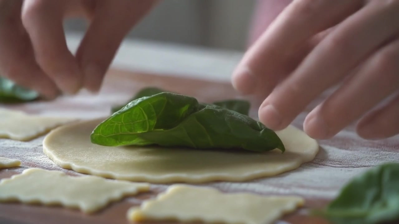 Chef che adagia foglie di spinaci freschi sull'impasto crudo della pasta