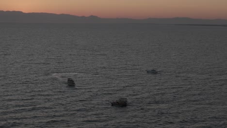 Small-boats-navigating-Mediterranean-sea-under-glowing-sunset-orange-skyline