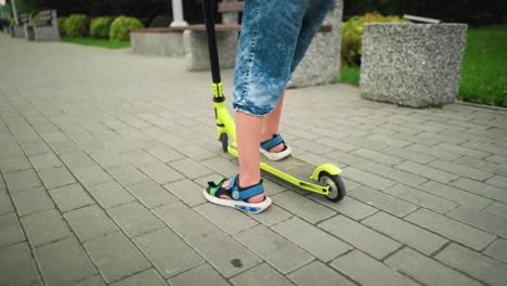 back view of a child riding a neon yellow scooter along a smooth interlocked pathway