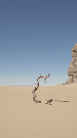 a dead tree stands in a desert landscape with a rock formation in the background