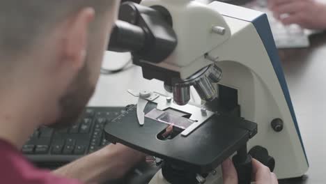 male microbiologist, medical worker looks at blood sample through a microscope, makes analysis in laboratory. laboratory assistant conducts histological research of biomaterial using modern microscope