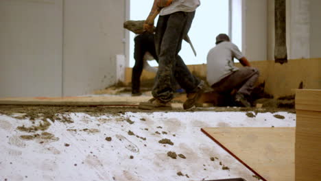 workers shape wet concrete with focus and intensity, kneeling and stretching across fresh material in a moment of raw, grounded construction energy.