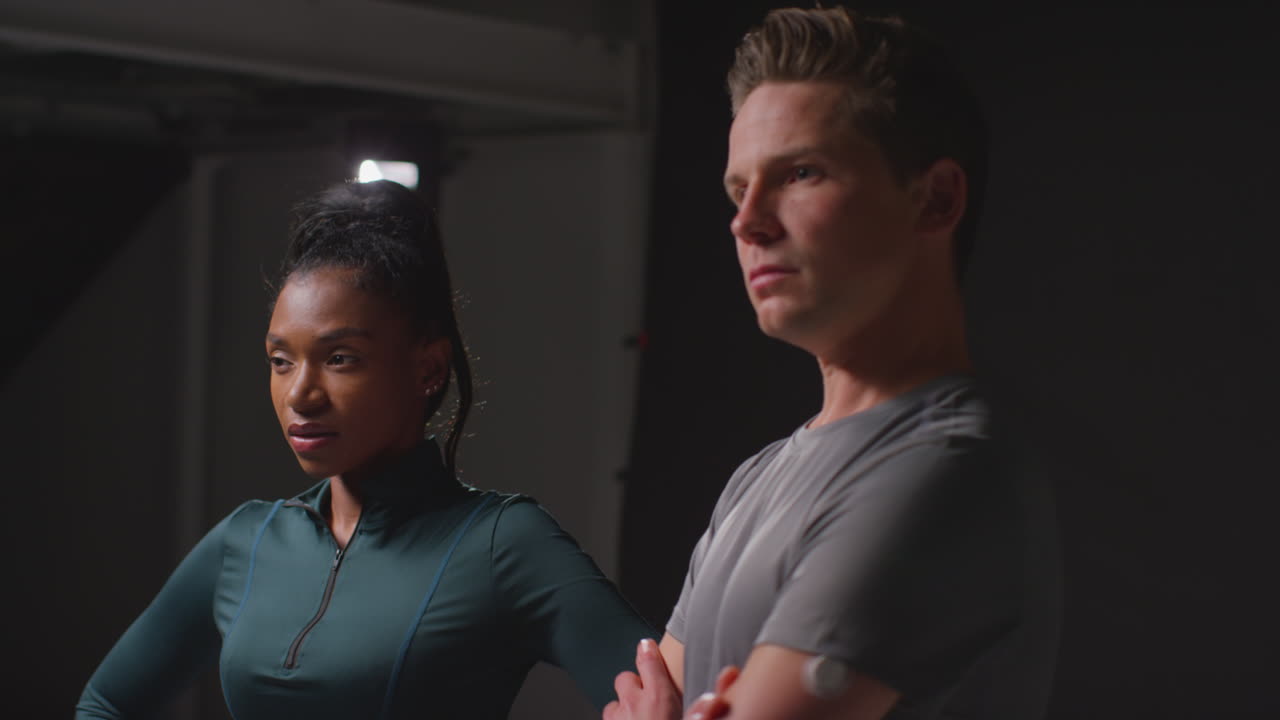 студийный портрет серьезной и решительной спортивной пары или друзей в фитнес-одежде, снятый в тренажерном зале при низком освещении