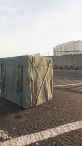 a large gray crate covered in a tarpaulin, sitting on a paved road.