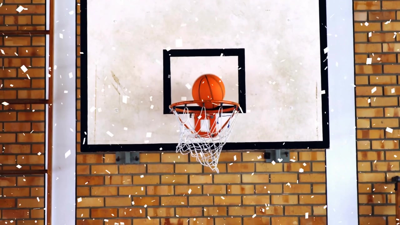 Basketball hoop and ball balancing on rim, confetti floating across brick gym wall