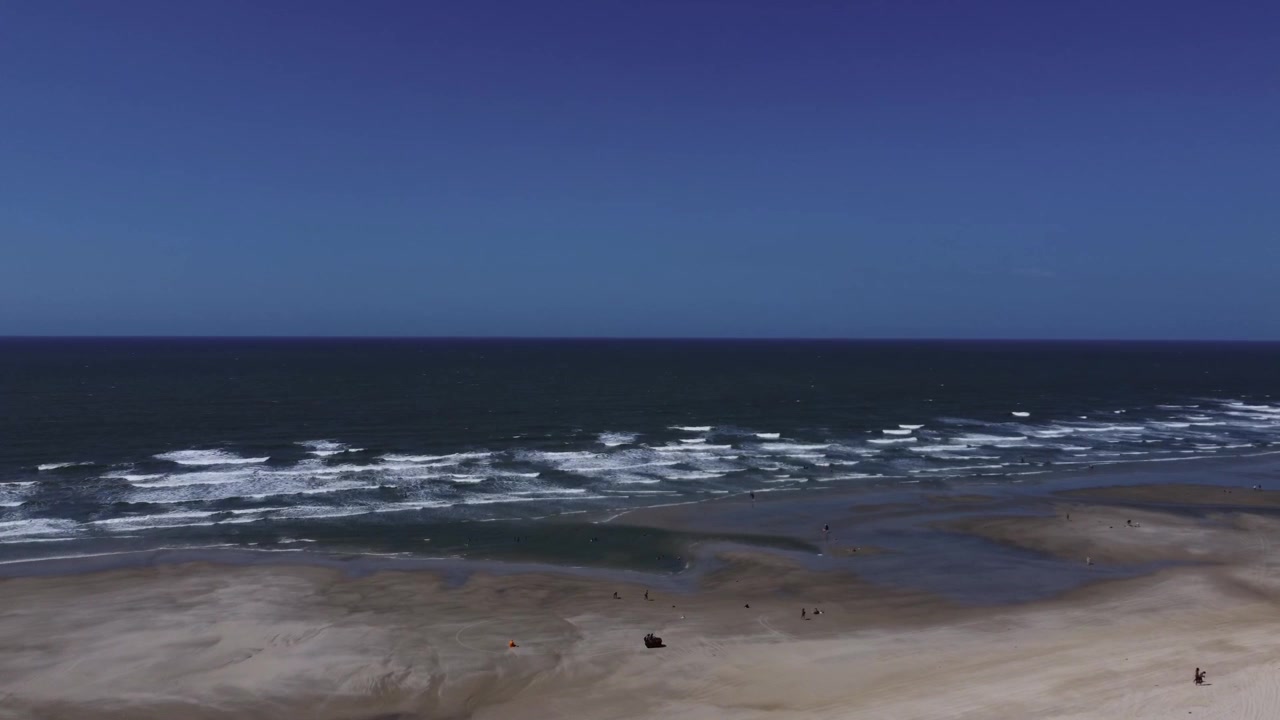 Højvinkel luftfoto af besøgende, der slentrer langs den brede sandbanke, mens havbølger bryder på stranden Caburé i Maranhão, Brasilien