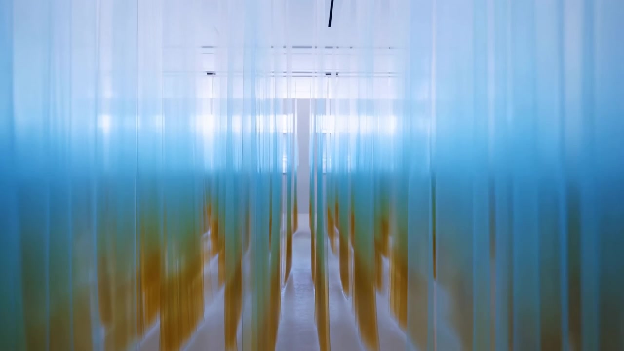 Passaggio interno astratto incorniciato da strisce verticali blu traslucide, che conduce verso un centro luminoso e illuminato con luci a soffitto bianche e soffuse e calde