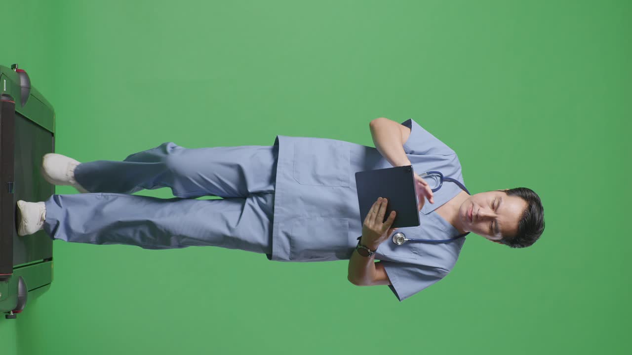 cuerpo lleno de médico masculino asiático con estetoscopio usando una tableta mientras camina en el fondo de la pantalla verde en el hospital