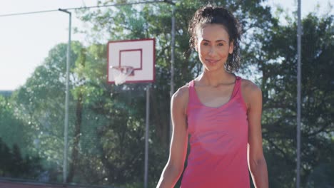 Happy-biracial-female-basketball-player-holding-ball-on-sunny-court,-copy-space,-slow-motion