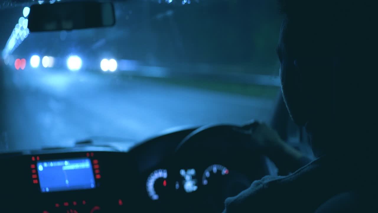 밤의 비가 오는 도로에서 차를 운전하는 젊은 남자