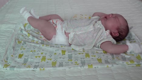 an adorable newborn baby lying in the bed stretches and starts to cry - close up