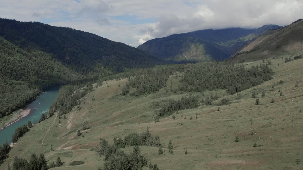 Ampie riprese aeree del fiume turchese che serpeggia attraverso la valle di Ak-Kem con pendii boscosi e montagne aspre sotto un cielo nuvoloso, Repubblica dell'Altai, Russia.