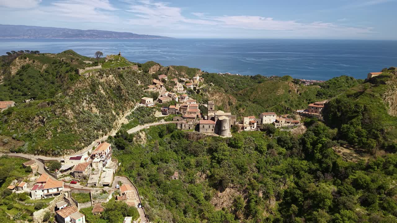 Luftfoto af bjerglandsbyen Savoca og Pentefur Slot på Sicilien, Italien, med hav i baggrunden.