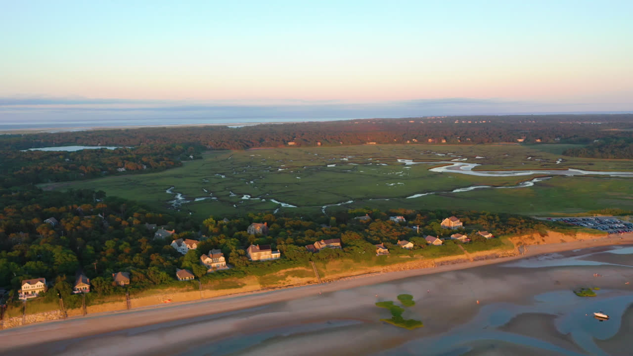 Filmagem aérea por drone da Baía de Cape Cod: Casas à beira-mar e marismas na maré baixa durante a hora dourada com gaivotas voando abaixo