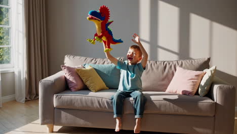 happy boy plays with colorful toy dragon on couch at home