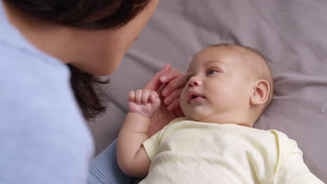 mother playing with baby son lying on bed in nursery