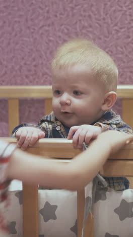active little girl jumps up and junior brother nibbles wooden cot edge in light children room at home closeup