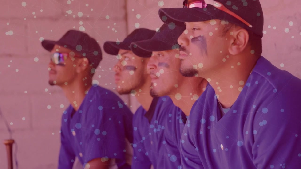 Inquadratura iniziale che mostra giocatori di baseball nel dugout rivolti verso il campo mentre guardano la partita sotto particelle fluttuanti