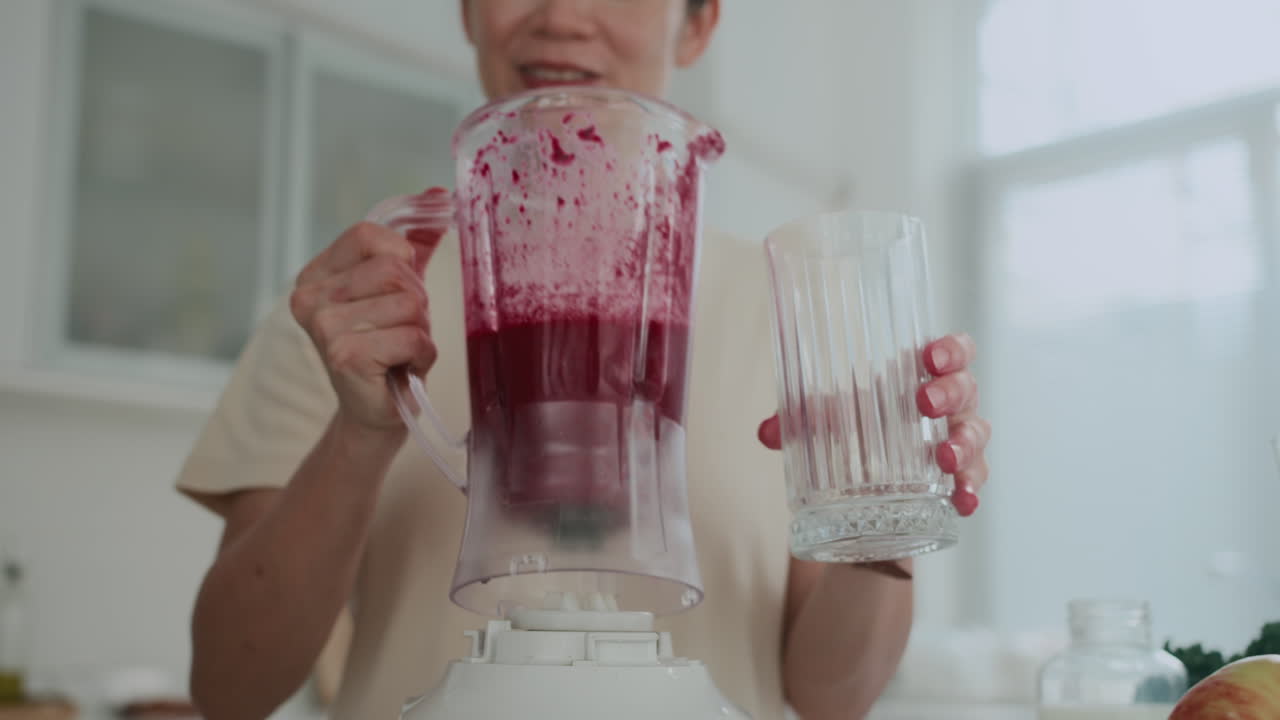 Woman Pouring Fruit Smoothie in Cup at Home Kitchen
