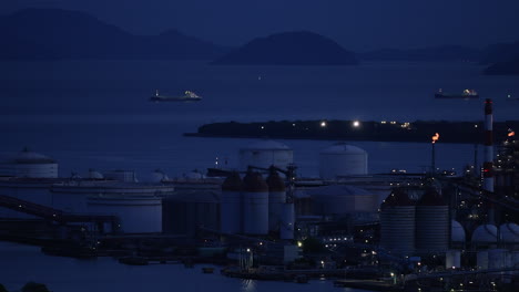 industrial plant with smoking chimneys and burning flare stacks at dusk