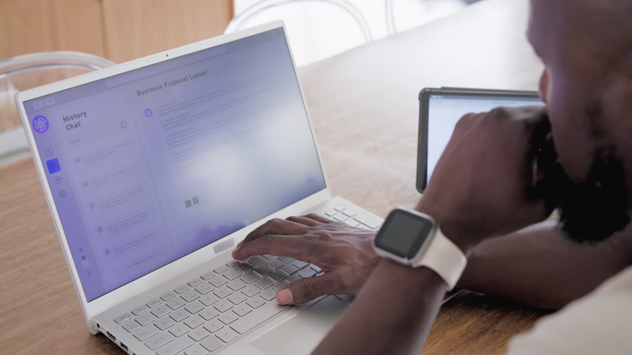 Vertical video: African man reviewing laptop, typing, clicking at table with tablet, copy space