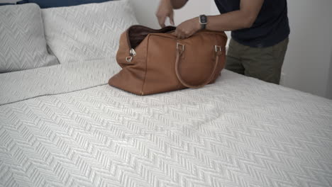 a man quickly packs clothes in a leather travel bag