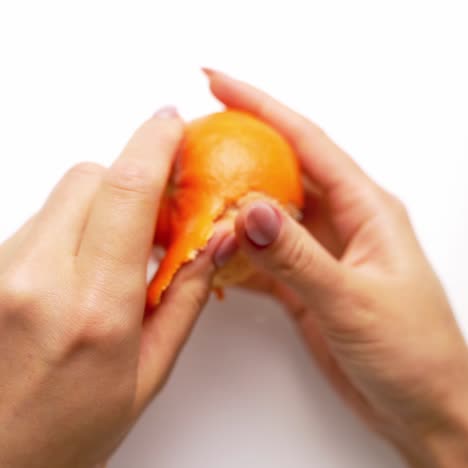 Woman cleans tangerine on the table. Top view of female's hands holds sweet citrus. Hands are peeling fresh mandarin. Close-up.