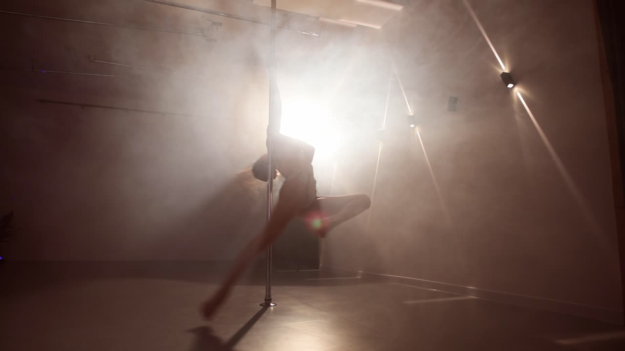 Vista statica di una giovane donna che fa pole dance su un palco fumoso