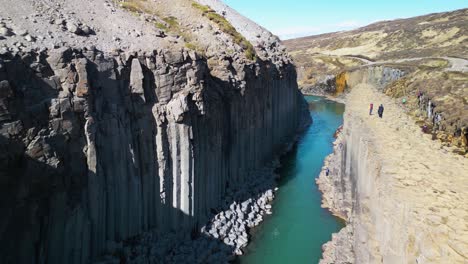 aerial drone forward moving shot over a winding river flowing through studlagil canyon with basalt columns in iceland on a sunny day