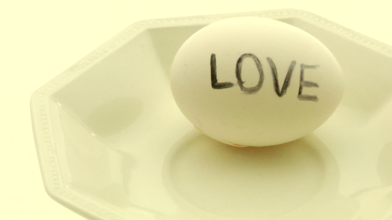 한 여성의 손이 사랑이라는 단어가 적힌 완숙 계란을 집어 깨뜨린다