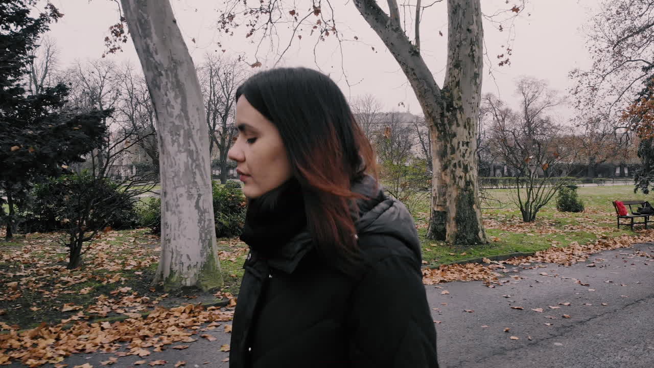 A sad young woman walks in a deserted park on a cloudy day